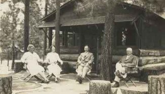 Black and white photo of Ayres family sitting outside of a log cabin